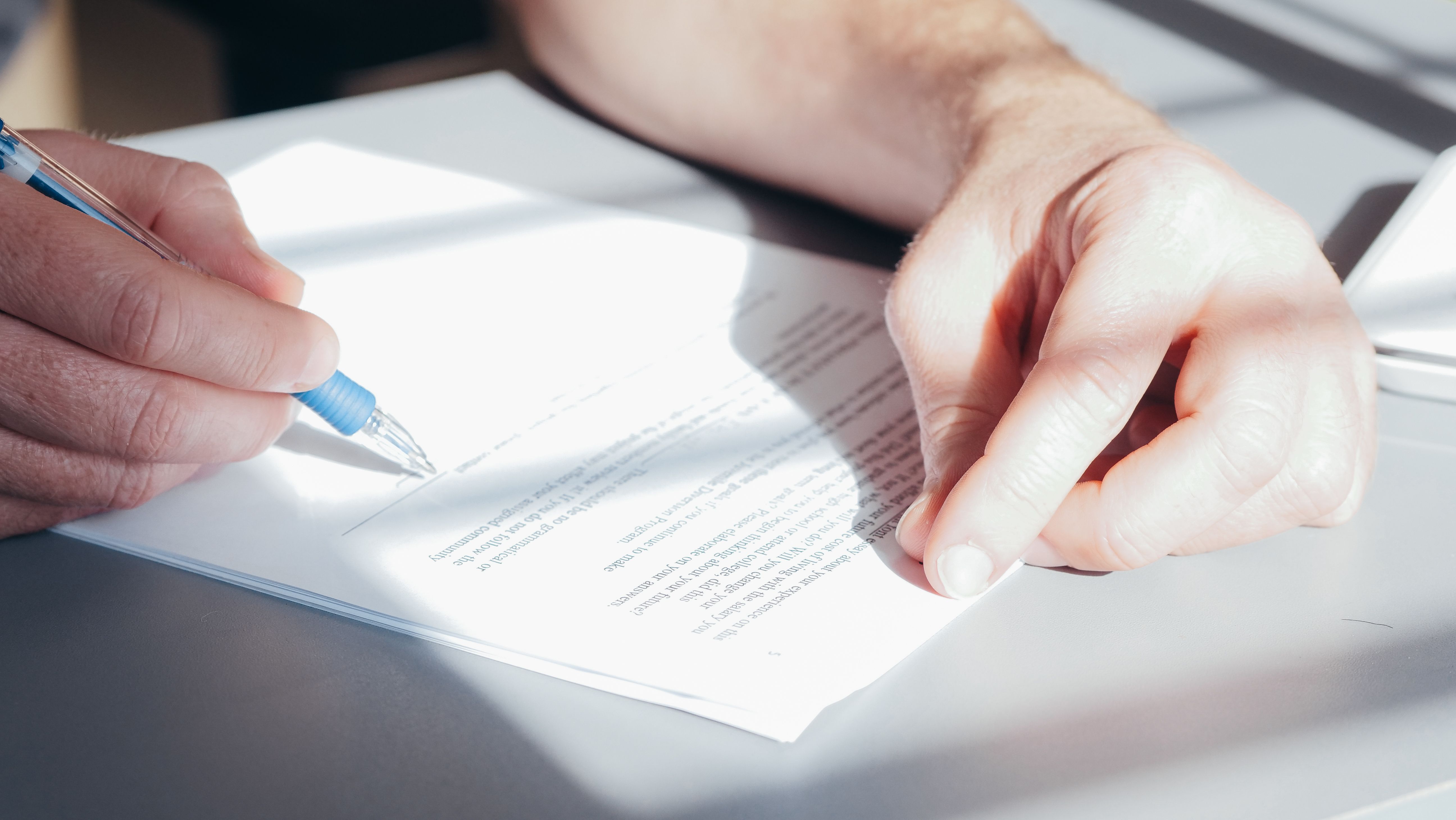Hands signing a contract with a blue pen, close-up view