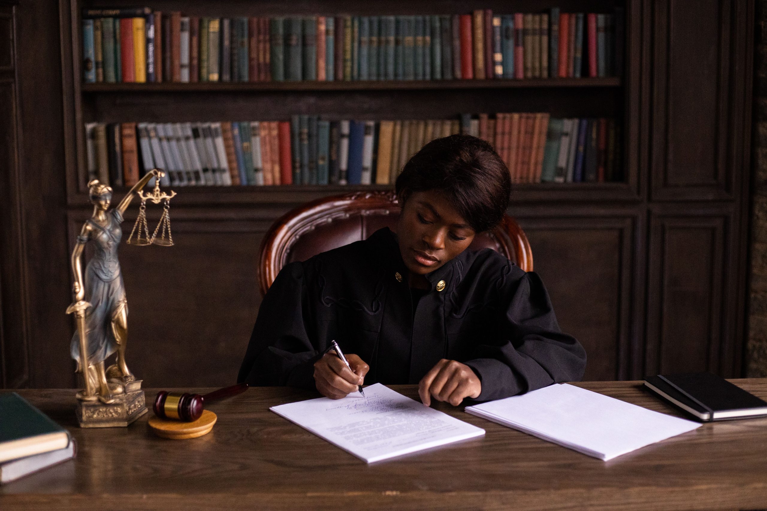 Judge in robes writing on a document at a desk in an office library with law books, representing complex litigation