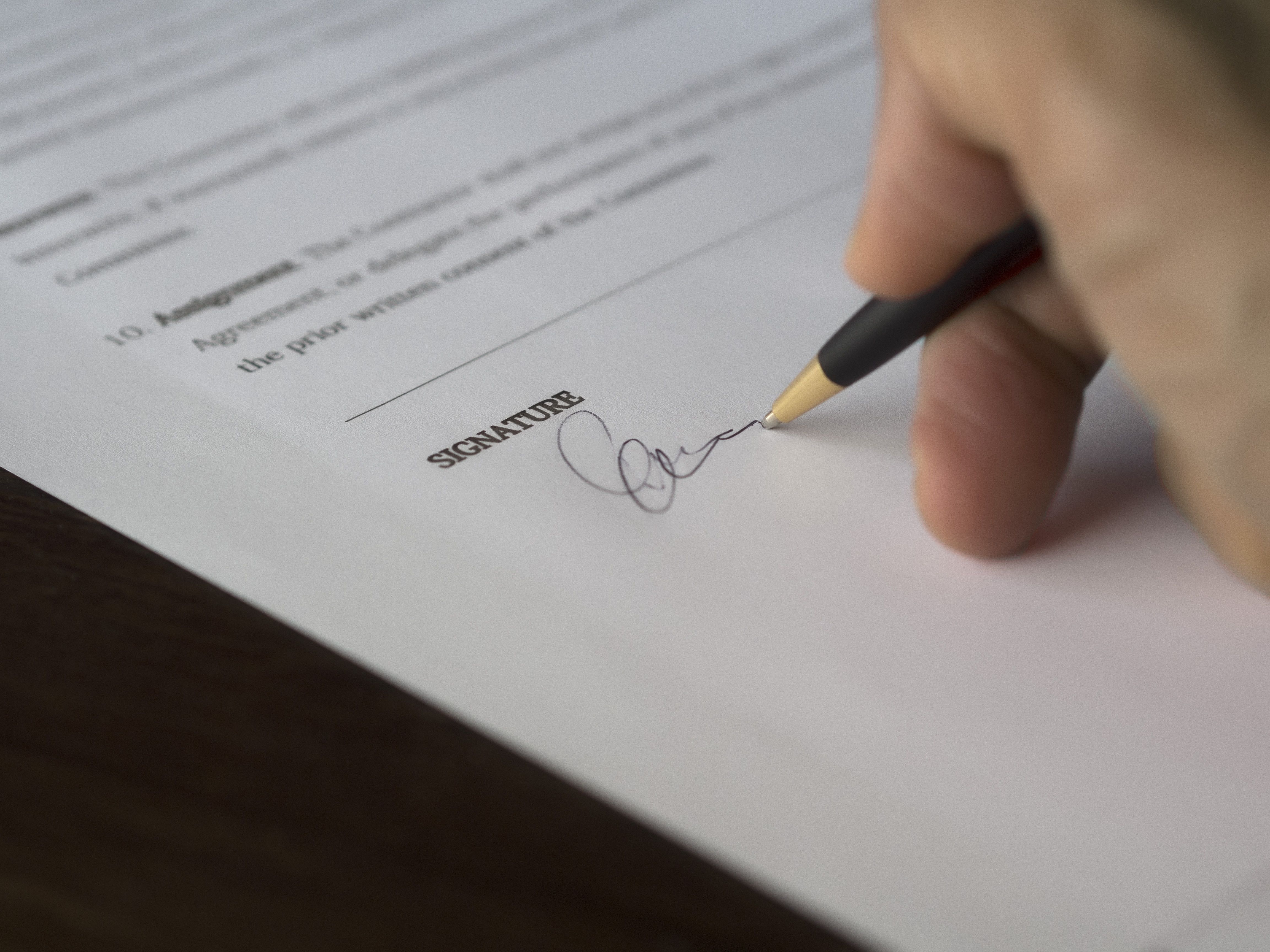 Hand signing a formal legal contract on a wooden desk
