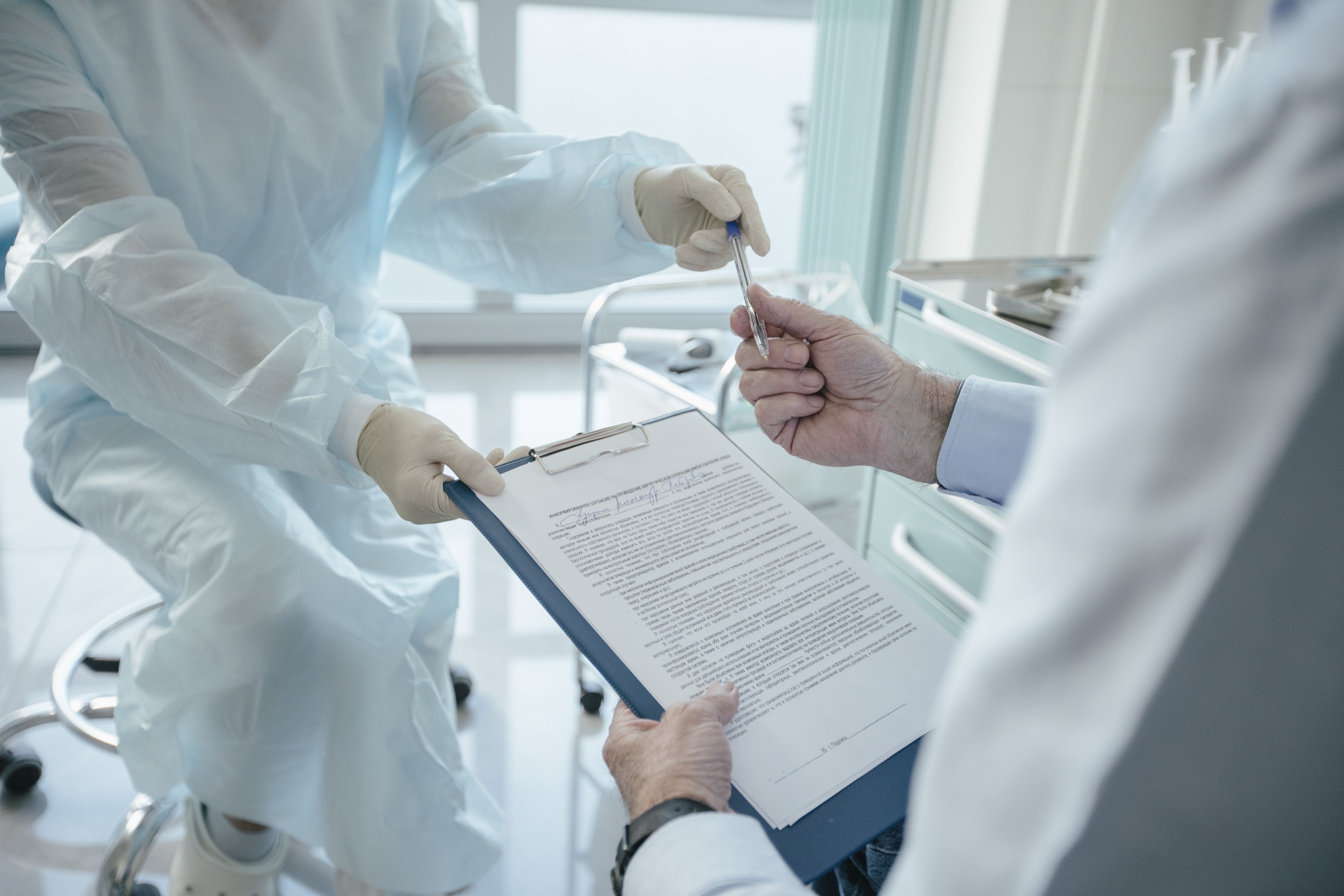 A doctor hands a clipboard to a patient for signature during a clinic visit